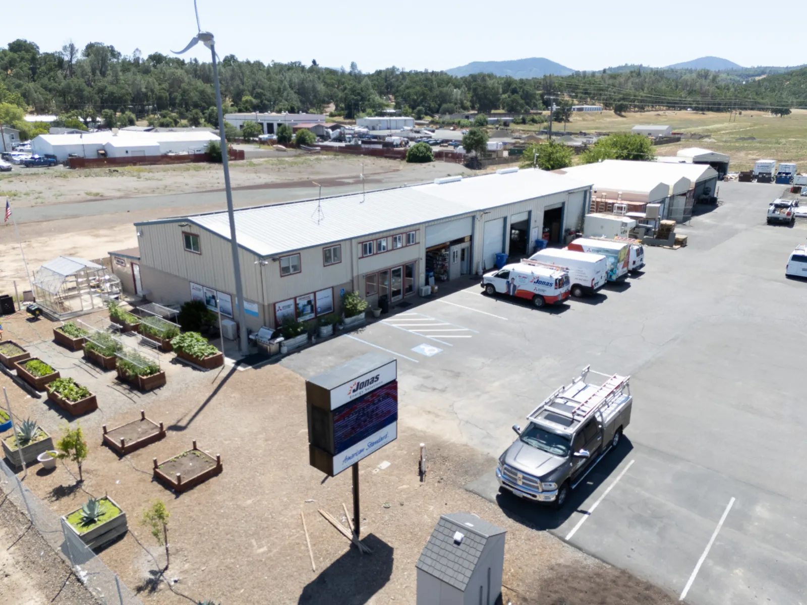 Aerial view of Jonas Energy Solutions headquarters in Lake County, featuring service vehicles, community garden beds, and surrounding landscape.