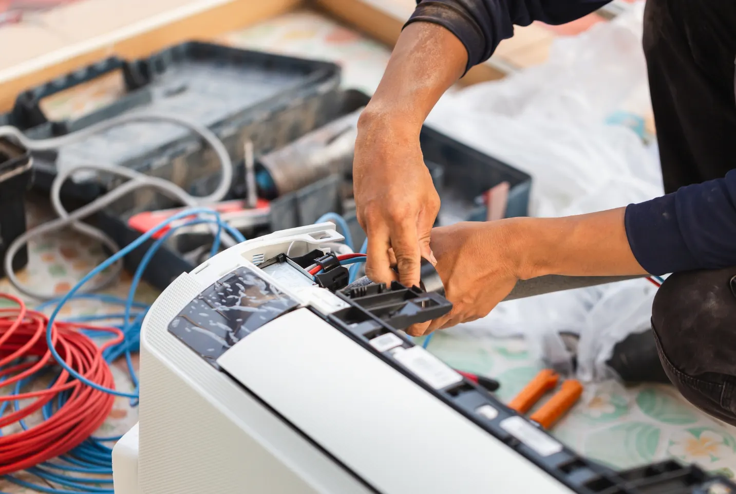 Close-up of a technician servicing an air conditioning unit with exposed wiring and tools laid out, demonstrating detailed HVAC maintenance work.