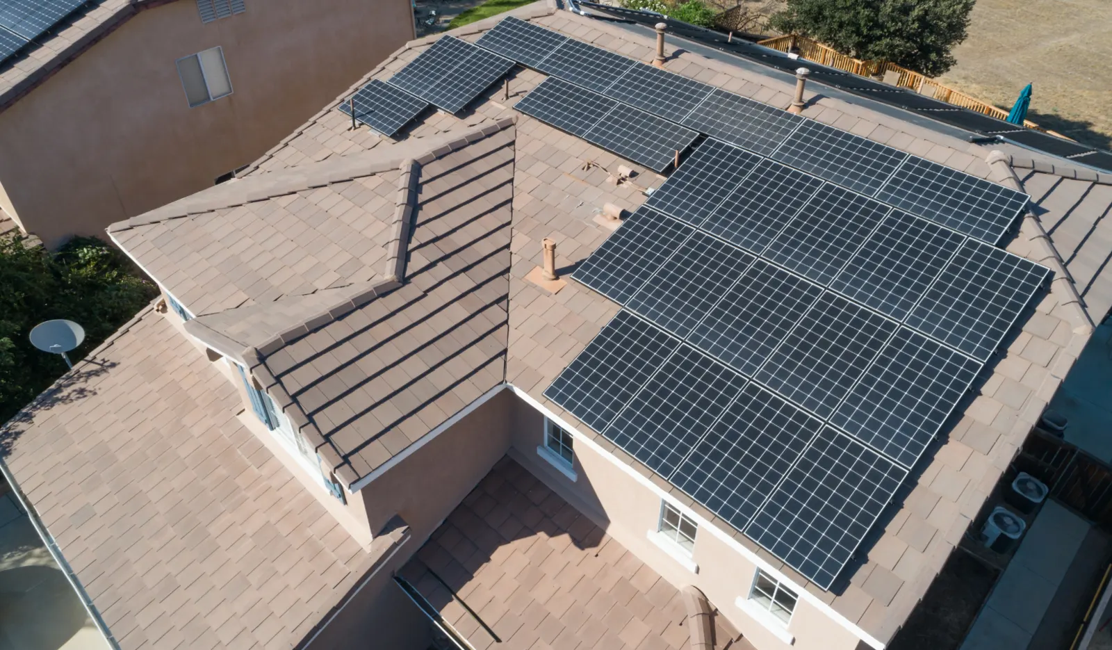 Aerial view of a residential home with a full solar panel system installed on a multi-angled tile roof for maximum energy efficiency.